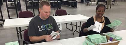 A male and female election worker sit at table opening ballot envelopes